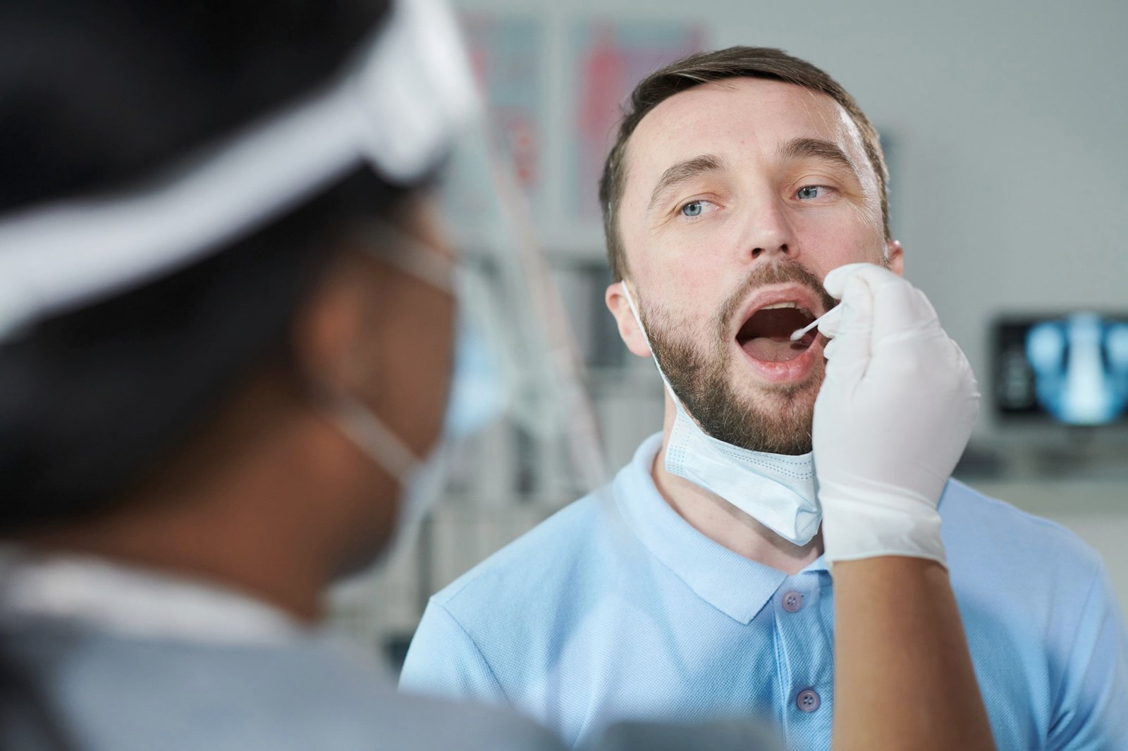 face-young-male-patient-with-open-mouth-looking-female-clinician-protective-workwear-while-being-tested-covid-with-oral-swab-clinics-min