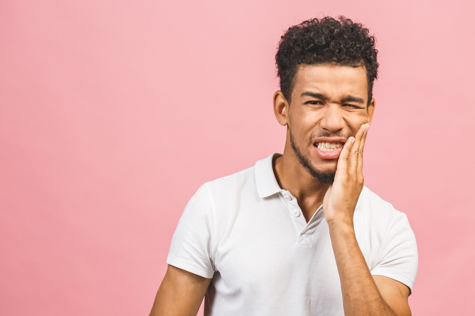 indoor-portrait-young-worried-african-american-male-isolated-white-background-dressed-casual-experiencing-strong-toothache-pressing-hand-chin-because-sore-jaws-min