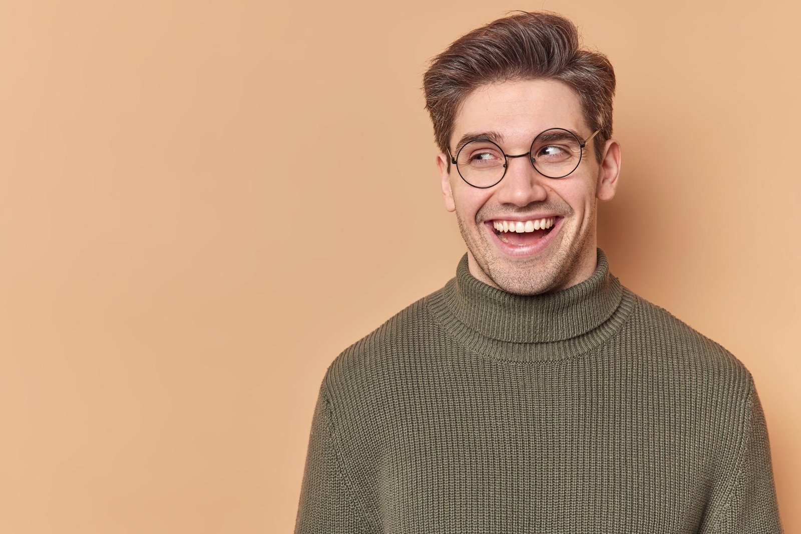 portrait-handsome-man-with-broad-sincere-smile-looks-away-feels-good-sees-something-funny-wears-round-eyeglasses-casual-jumper-isolated-beige-background-with-copy-space-your-advertisement
